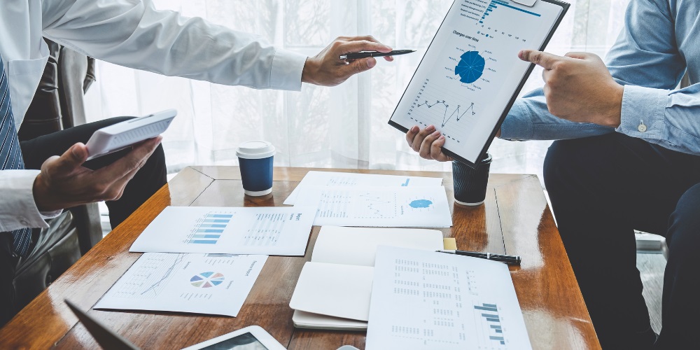 Two people pointing at a graph amidst a pile of papers