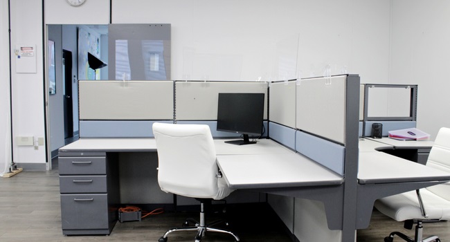 Two cubicles sharing a retaining wall with a white office chair in front of each