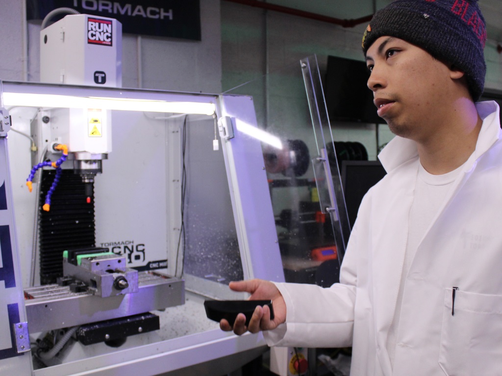 A man wearing a lab coat standing in front of a CNC machine