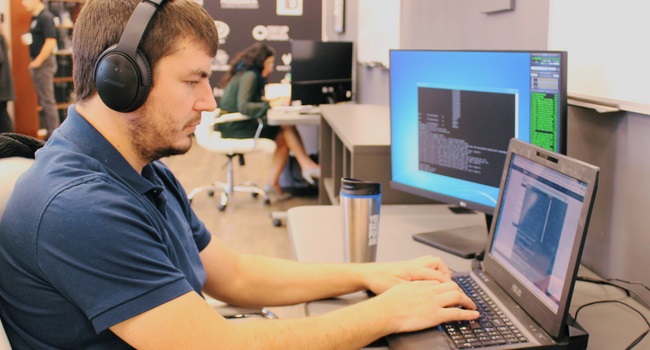 A man sitting at a laptop and desktop computer screen while wearing headphones