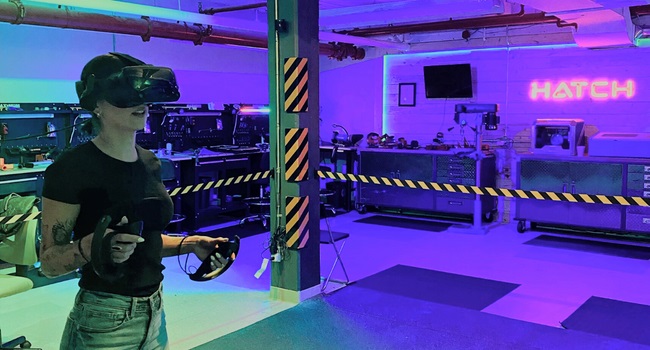 A woman wearing a VR headset and holding controllers while standing in a taped off area