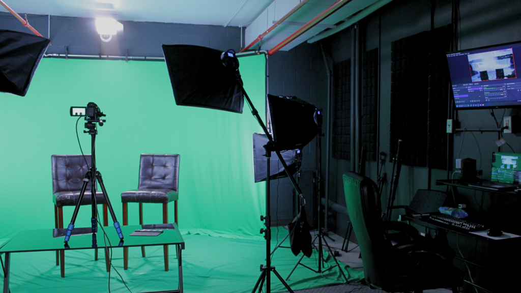 Multimedia photography studio with green screen set up. Professional lighting and interview chairs are present on the greenscreen set.
