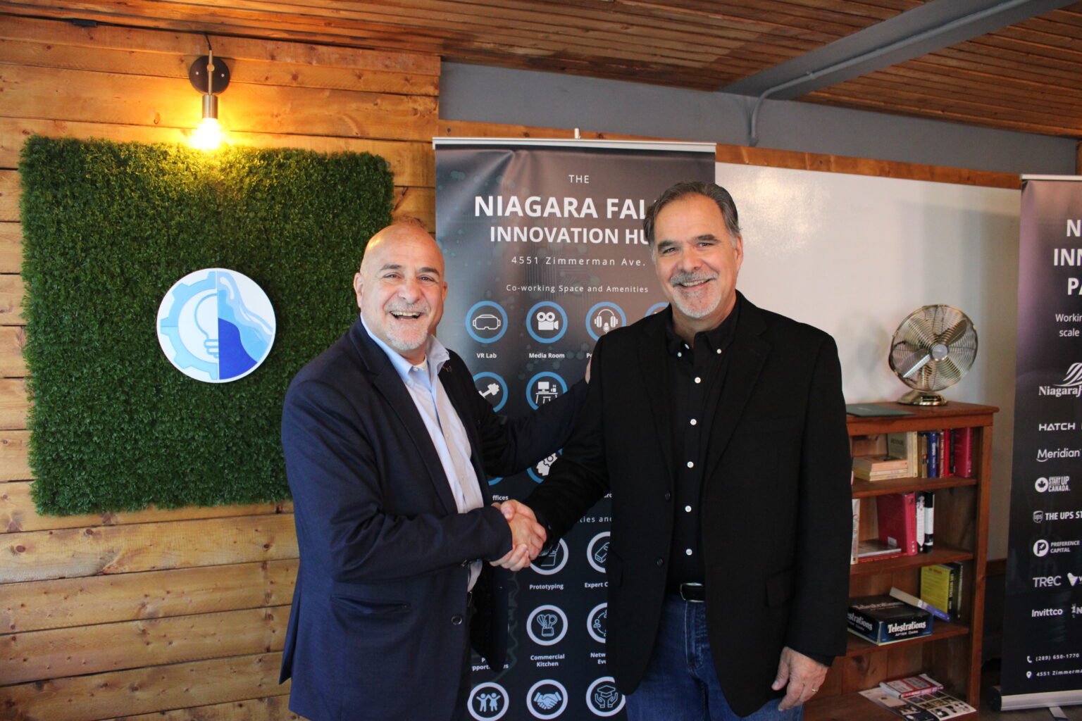 Two men smiling and shaking hands in front of a banner in the Think Tank