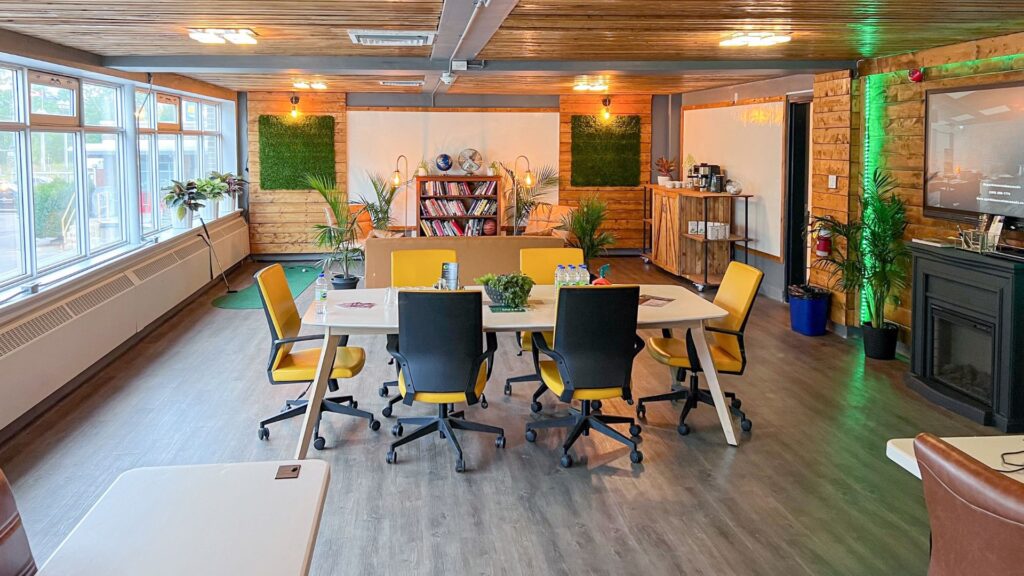 A meeting room at the Innovation Hub. Yellow chairs surrounding a large table in a spacious room. Behind the table is a bookcase and an open seating area for collaboration.