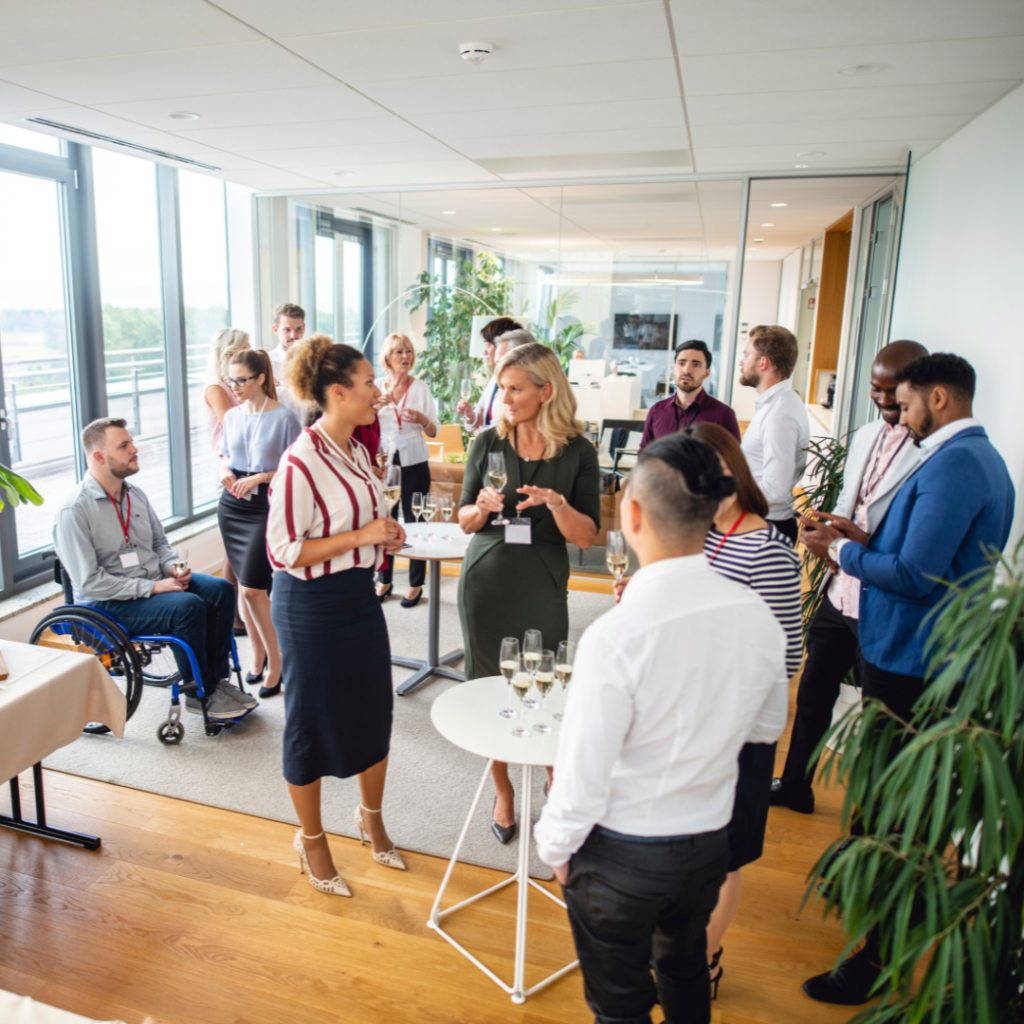 People celebrating a launch event. Corner angle with glasses of a bubbly beverage on a table. People all standing around table and talking with each other.