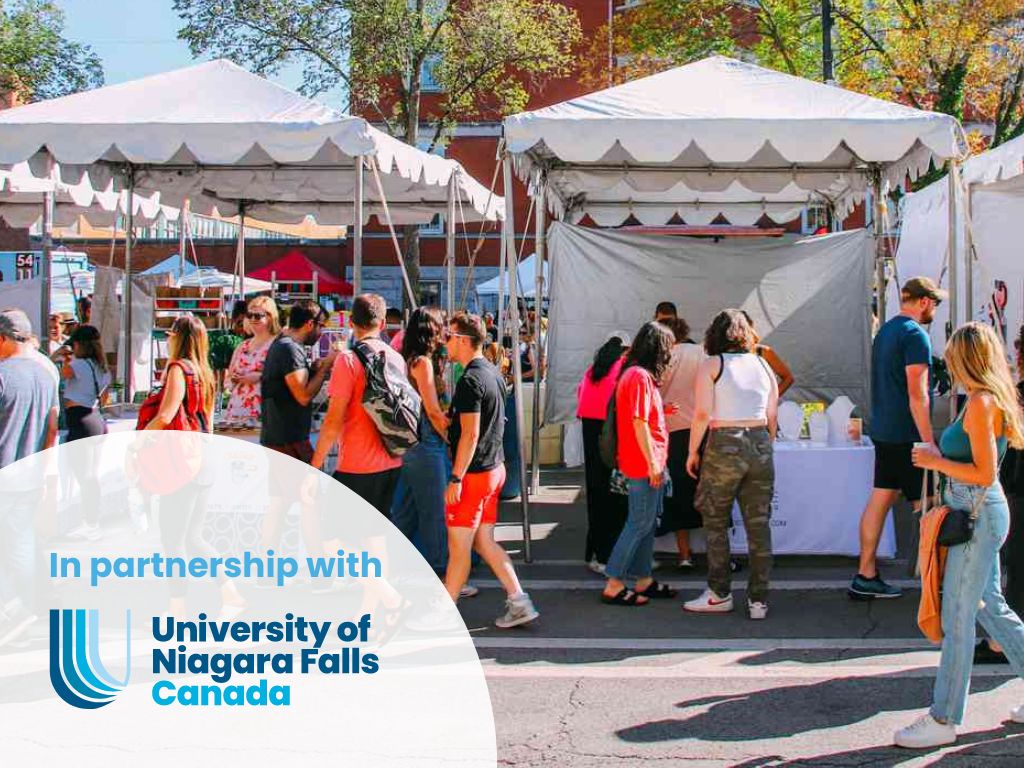 Outdoor farmers market with retail vendors. Attendees are walking the street looking at vendor's wares. the setting is a Fall day. In the bottom left corner of the image the partnership logo is present, The University of Niagara Falls Canada